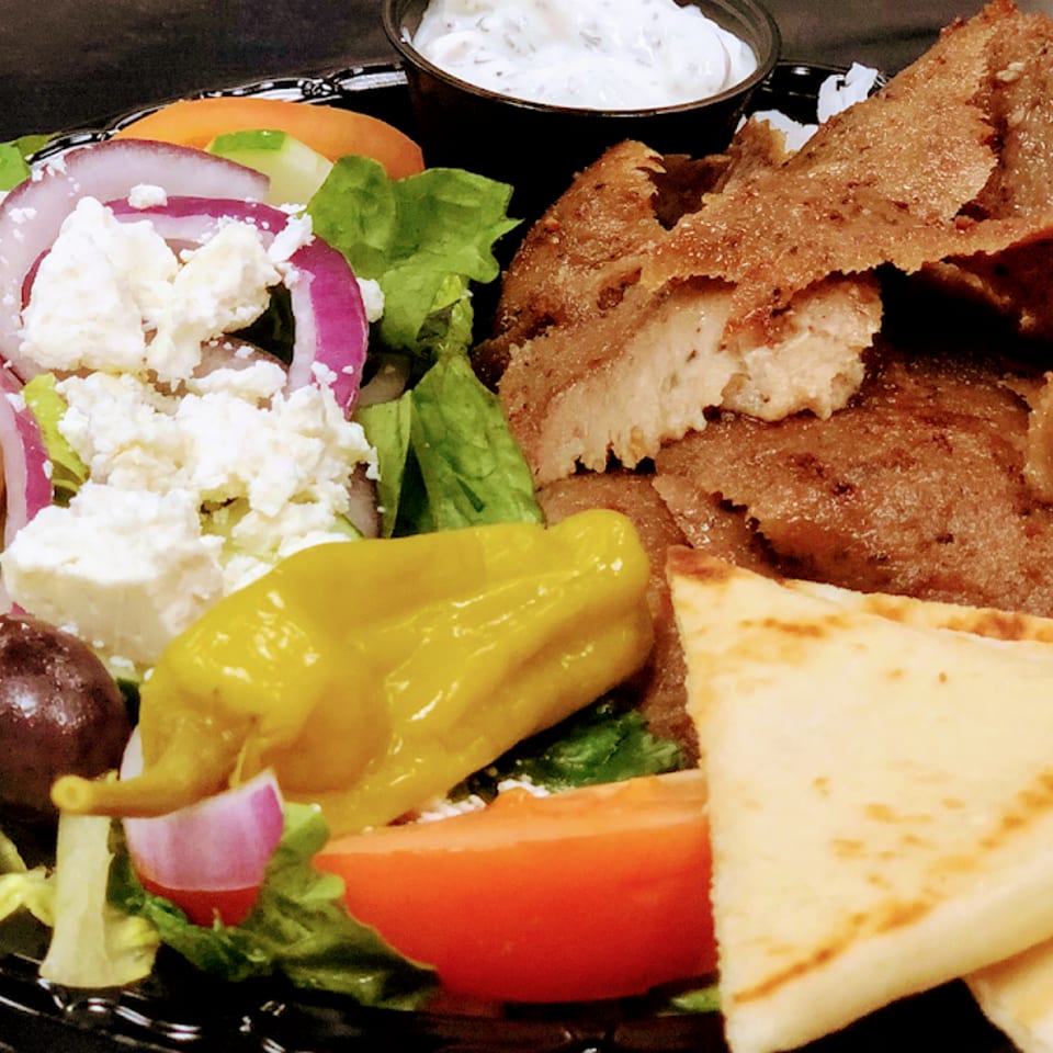 A gyro platter with sliced meat, Greek salad, pita bread, and tzatziki sauce.