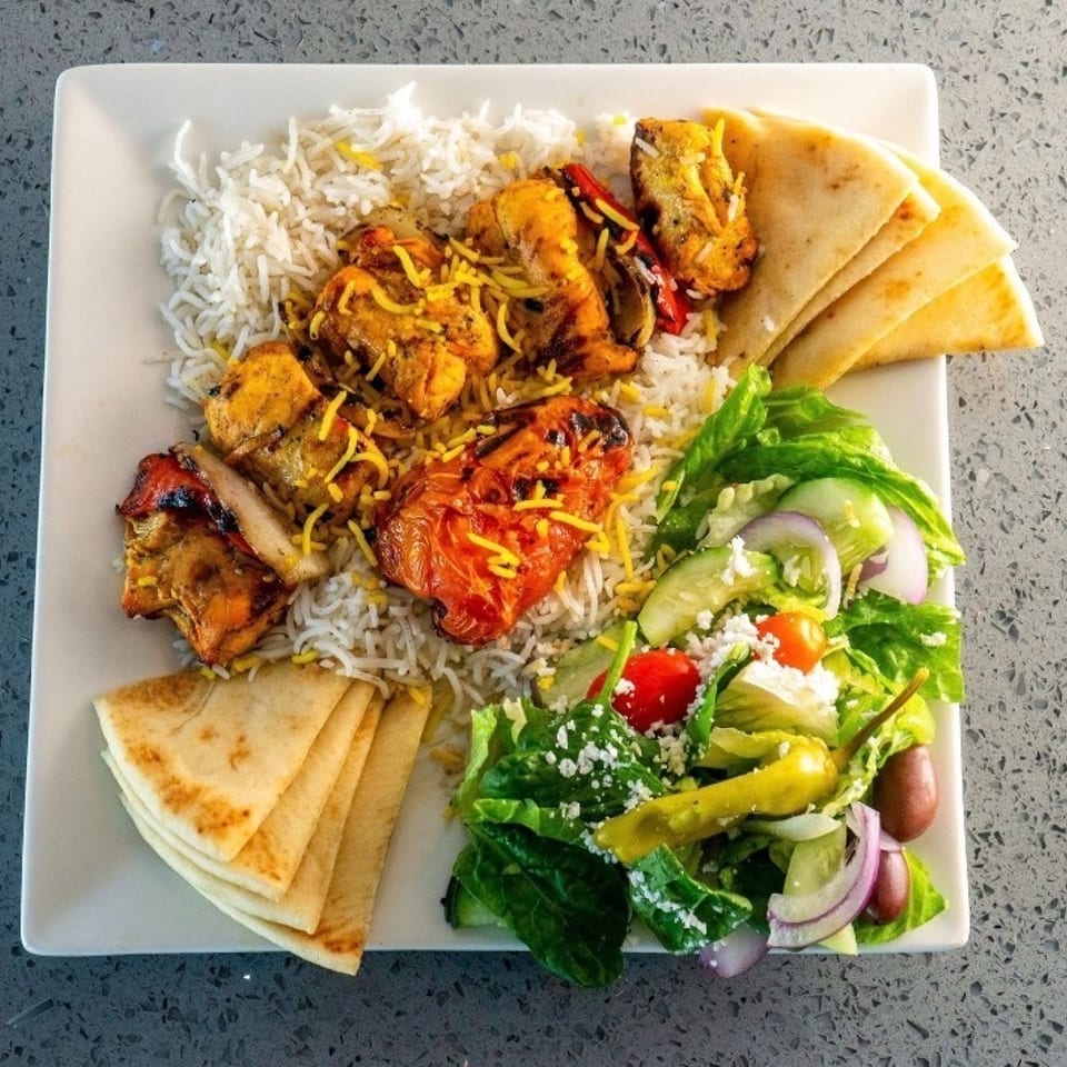 Plate of fragrant rice topped with grilled chicken, roasted tomato, flatbread, and fresh Greek salad.