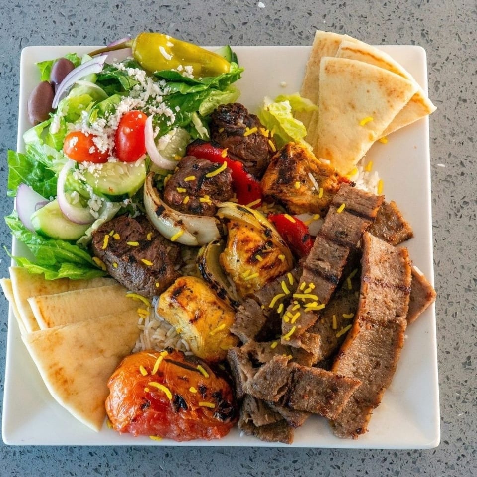 Mediterranean mixed grill platter with grilled meats, roasted vegetables, rice, pita bread, and Greek salad.